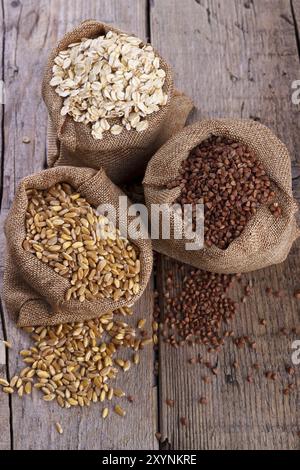 Cereali per una dieta sana, grano, farina d'avena e grano saraceno in sacchi su fondo rustico in legno Foto Stock