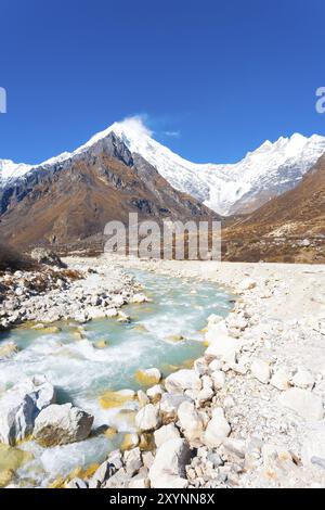 Roccioso terreno arido paesaggio linee a che scorre veloce sul ghiacciaio del fiume di acqua con Himalayan mountain range, Langtang Lirung peak, in background in alto alt Foto Stock