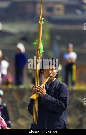 Xijiang, Cina, 15 settembre 2007: Miao, un uomo di minoranza etnica che suona un alto strumento di flauto di bambù in un festival nella piazza della città nella villa di Miao Foto Stock