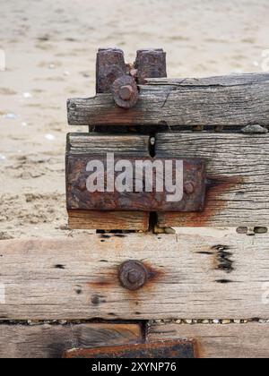 dettaglio ravvicinato di dadi in metallo arrugginiti bulloni rondelle raccordi su legno di legno con spiaggia sabbiosa sullo sfondo Foto Stock