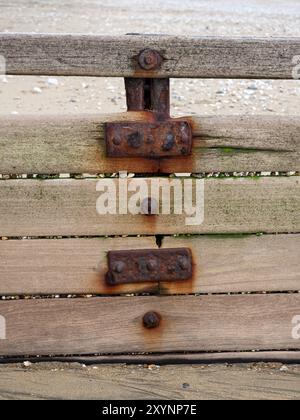 dettaglio ravvicinato di dadi in metallo arrugginiti bulloni rondelle raccordi su linee in legno di legno con spiaggia sabbiosa sullo sfondo Foto Stock