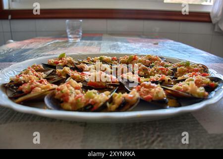 Primo piano di un piatto di cozze appena preparate e condite con un vivace condimento di vinaigrette. Il piatto è ben presentato con verdure tritate Foto Stock