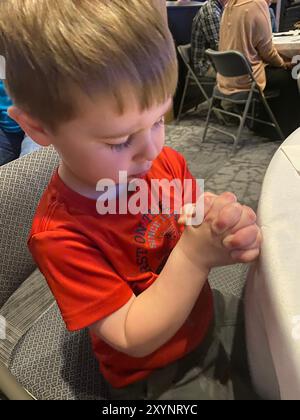 Ragazzo di quattro anni che inchina la testa con le mani piegate e gli occhi chiusi pregando in chiesa Foto Stock