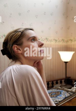 Giovane donna seduta ad una scrivania antica con un'espressione premurosa. formato verticale. Giovane donna seduta su un'antica scrivania con espressione penosa. Foto Stock