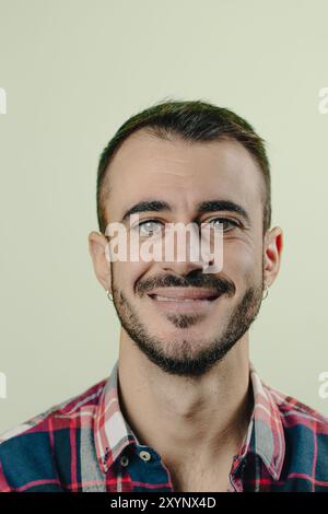 Il giovane con la barba e una camicia a quadri sorride su uno sfondo verde Foto Stock