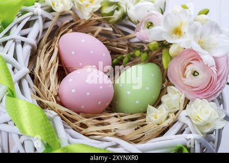 Cesto di uova di pasqua con fiori di colore bianco su sfondo di legno Foto Stock