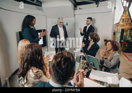 Il team aziendale diversificato sta applaudendo un senior manager dopo una presentazione di successo in un ufficio moderno Foto Stock