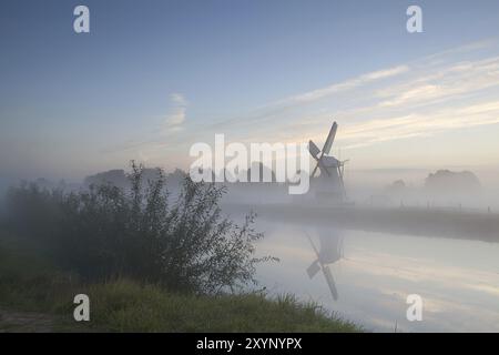 Mulino a vento sul fiume nella nebbia mattutina, Olanda Foto Stock