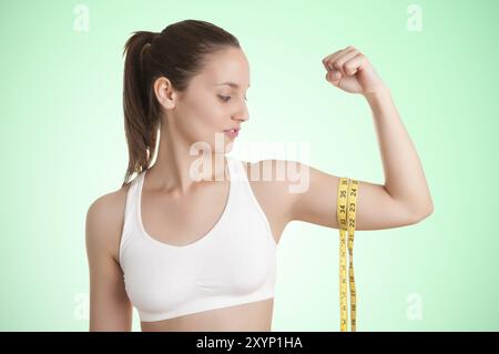 Potente donna misurando il suo bicipite con un giallo nastro di misurazione in uno sfondo verde Foto Stock