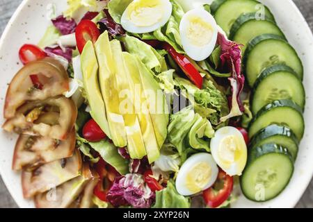 Cucina sana e concetto di dieta mediterranea piatto con piatto bianco con foglie di insalata di lattuga, uova di quaglia, avocado, pomodoro nero, cetriolo a fette, Foto Stock