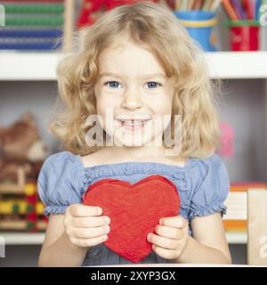 Felice bambino sorridente che tiene in mano il cuore di carta rossa. Il concetto di San Valentino Foto Stock