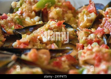 Primo piano sui vivaci dettagli delle cozze serviti con un colorato condimento di vinaigrette. Ogni guscio di cozze è abbondantemente ricoperto con un mix di t tritate Foto Stock