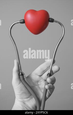 Mano d'uomo tenendo un cuore rosso e uno stetoscopio Foto Stock