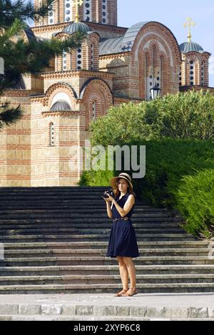 Turista femminile vicino al monastero di Hercegovacka Gracanica a Trebinje: Una donna si trova con una macchina fotografica professionale sullo sfondo di una chiesa Foto Stock