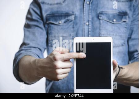 Uomo casual con camicia in denim che mostra lo schermo di un tablet digitale in mano. Isolato su bianco. Percorso di ritaglio per la visualizzazione incluso. Punta un dito A. Foto Stock