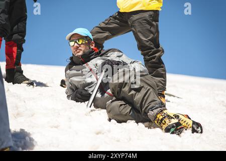 Allenamento per correggere lo scivolamento su un pendio o su un ghiacciaio con l'aiuto di un'ascia di ghiaccio. Una giovane guida con la barba spiega al suo gruppo come rallentare correttamente il Foto Stock