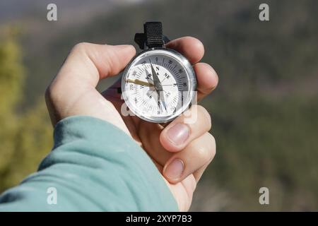 Primo piano UNA mano dell'uomo tiene una bussola tascabile sullo sfondo di montagne e boschi. Il concetto di navigazione all'aperto Foto Stock