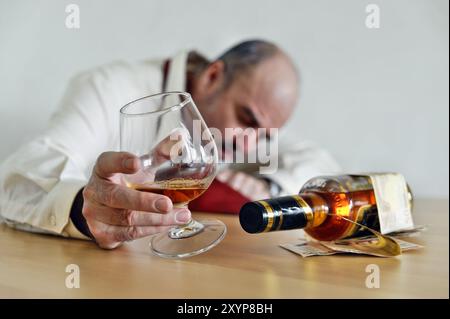 Alcolico siede a tavola con un cecchino di cognac e una bottiglia di schnapps Foto Stock