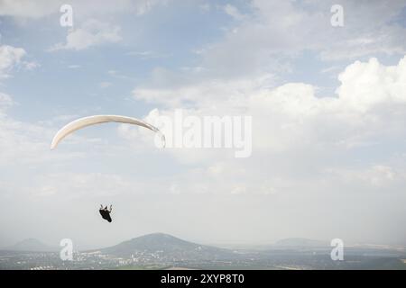 Un parapendio bianco-arancio vola sul terreno montuoso Foto Stock