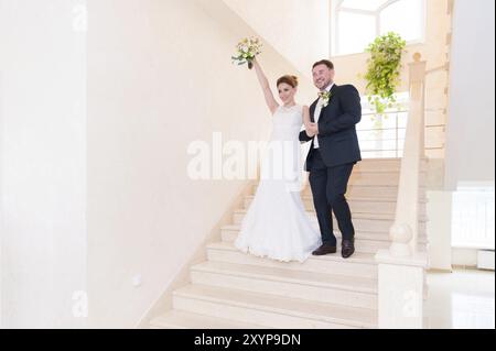 Un paio di sposi novelli scendono le scale nell'ufficio del registro e salutano coloro che li incontrano con sorrisi e gesti. Il concetto di matrimonio in Th Foto Stock