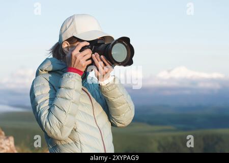 Ritratto di una fotografa di ragazza in un cappello sulla natura che fotografa sulla sua fotocamera digitale a specchio. Vista frontale Foto Stock