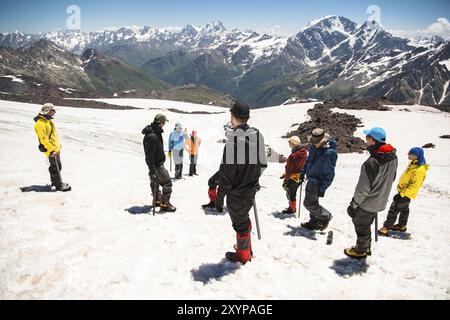 Allenamento per correggere lo scivolamento su un pendio o su un ghiacciaio con l'aiuto di un'ascia di ghiaccio. Una giovane guida con la barba spiega al suo gruppo come rallentare correttamente il Foto Stock