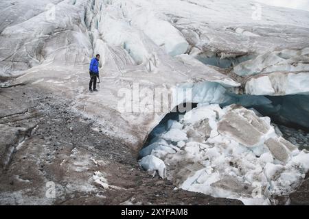 Il viaggiatore in una cuffia e gli occhiali da sole è seduto nelle montagne innevate sul ghiacciaio. Viaggiatori in un ambiente naturale Foto Stock