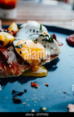 Una colazione vibrante comprende un uovo ben cucinato con il lato soleggiato sopra una pancetta croccante, guarnito con erbe e ingredienti freschi su un blu brillante PL Foto Stock