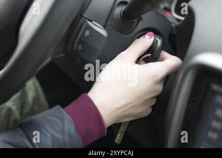 Primo piano interno veicolo di mano in possesso della chiave di accensione, il volante e il nero di fondo interna femmina, il concetto di driver Foto Stock