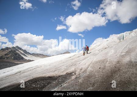 Due turisti, un uomo e una donna con zaini e gatti in piedi, stanno sul ghiaccio sullo sfondo delle montagne del cielo e delle nuvole. Foto Stock