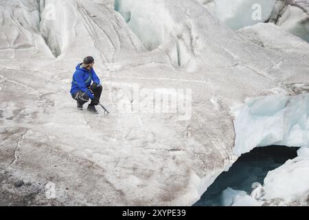 Il viaggiatore in una cuffia e gli occhiali da sole è seduto nelle montagne innevate sul ghiacciaio. Viaggiatori in un ambiente naturale Foto Stock