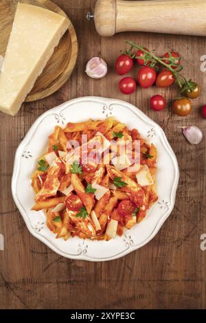 Foto in alto di un piatto di pasta con pollo e salsa di pomodoro. Penne con ingredienti, pomodori ciliegini e spicchi d'aglio, con consistenza rustica scura wi Foto Stock