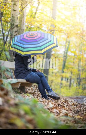 Giovane ragazza in blue coat e ombrello è una passeggiata attraverso la foresta autunnale Foto Stock