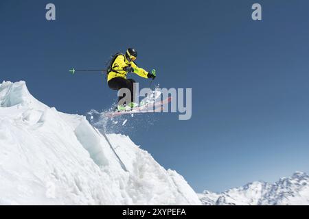 Uno sciatore con attrezzatura sportiva completa salta nel precipizio dalla cima del ghiacciaio sullo sfondo del cielo blu e della neve caucasica Foto Stock