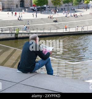 Un uomo siede su un gradino nel quartiere governativo di Berlino e legge la sezione finanziaria di un giornale Foto Stock