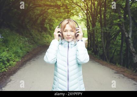 Ritratto di una bella giovane donna che tiene le cuffie ascoltando musica all'aperto nella foresta. Musica gioiosa Foto Stock