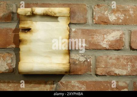 Vecchio pezzo di pergamena con bordi bruciati su un muro di mattoni, sfondo grintoso Foto Stock