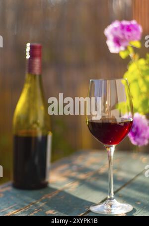 Un bicchiere di vino rosso su un vecchio tavolo rustico in legno. Godendole nel giardino privato al sole della sera Foto Stock