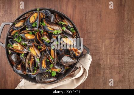 Cozze alla marinara, moules mariniere, in una grande padella di cottura, overhead shot al buio su un rustico sfondo di legno Foto Stock