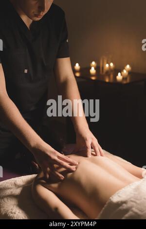 Le mani degli uomini fanno un massaggio terapeutico al collo per una ragazza sdraiata su un lettino massaggiante in una spa con illuminazione scura. Primo piano. Tasto scuro Foto Stock