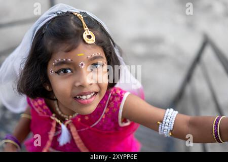 Una ragazza allegra che indossa abiti tradizionali colorati e gioielli decorativi sta salendo le scale, mostrando gioia ed eccitazione durante un festival locale Foto Stock