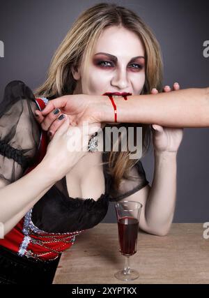 Donna bionda inventata come vampiro ad Halloween mentre beveva sangue dal braccio Foto Stock