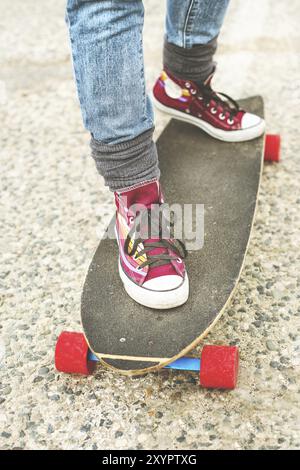 Dettaglio skateboard parzialmente grande con le gambe di una donna in sneakers Foto Stock