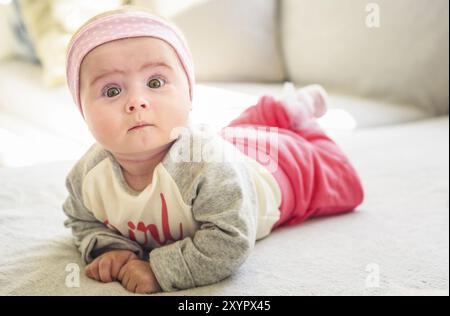 bambina di 6 mesi sdraiata su un divano in un luminoso soggiorno soleggiato. Concetto infantile Foto Stock