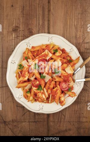 Un overhead foto di un piatto di pasta penne con pollo e salsa di pomodoro con una forchetta e un cucchiaio immerso nel piatto, girato da sopra al buio su un ru Foto Stock