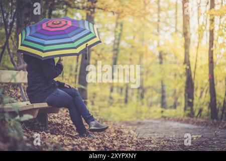 Giovane ragazza in blue coat e ombrello è una passeggiata attraverso la foresta autunnale Foto Stock