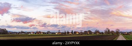 Panorama, tramonto sui campi e villaggio austriaco con cielo drammatico e nuvole colorate Foto Stock