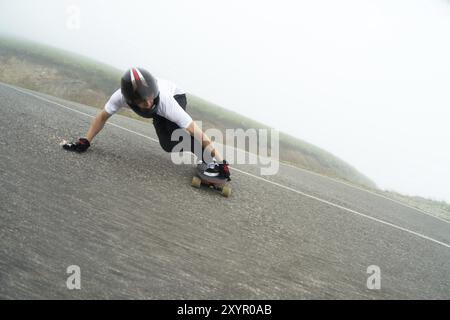 Un giovane con un casco integrale su una strada di campagna in uno scivolo passa una svolta su uno sfondo di nuvole basse e nebbia Foto Stock