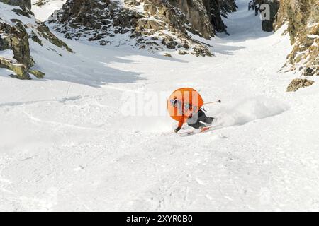 Uno sciatore freerider maschile con la barba scende dal fondo ad alta velocità dalla pista, lasciando una pista di neve con l'antivalanica aperta Foto Stock