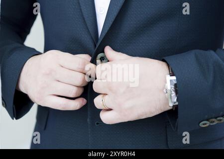 Uno stalwart nuvolato con una barba in un abito stringe il bottone della sua giacca. Primo piano eccellente. Il concetto di business style durante le vacanze Foto Stock